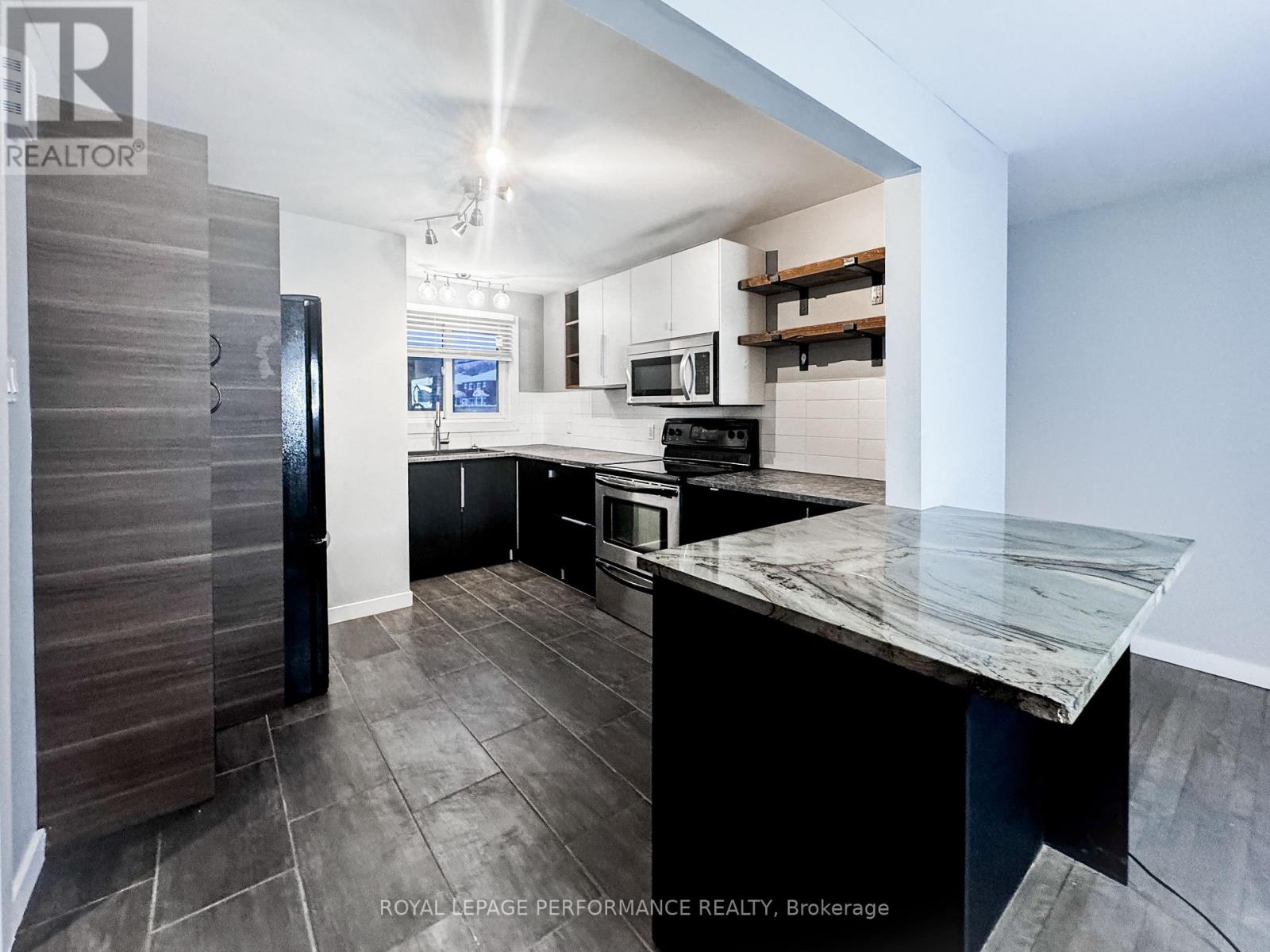 A modern kitchen with a marble countertop and a refrigerator with a wooden door.