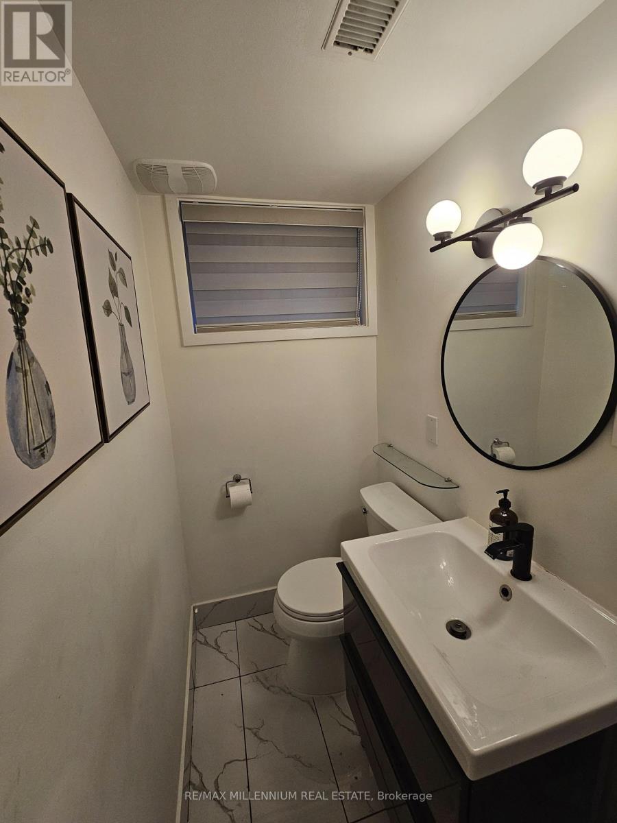 A bathroom with a toilet, sink, mirror and lighting.