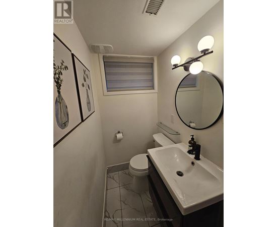 A bathroom with a toilet, sink, mirror and lighting.