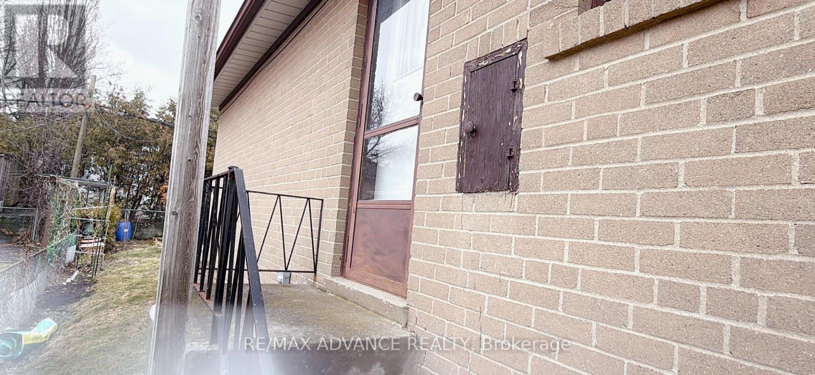 A brick wall with a small square window and a black metal railing.