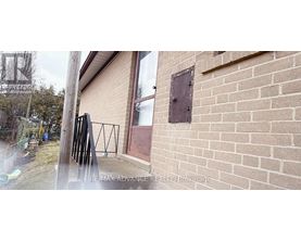 A brick wall with a small square window and a black metal railing.