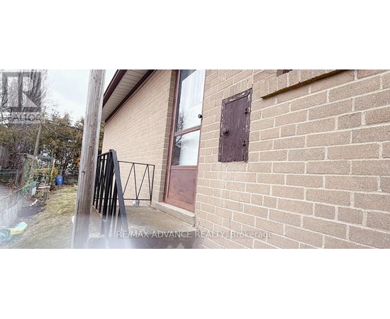 A brick wall with a small square window and a black metal railing.