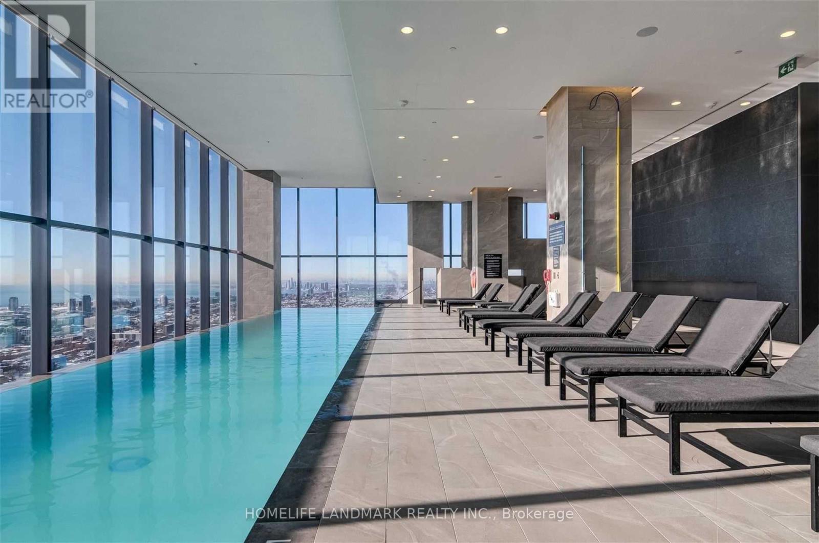 A long row of sun loungers are lined up by a swimming pool.