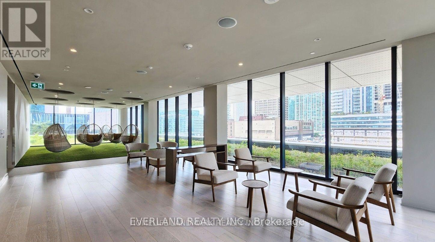 A spacious room with wooden floors and furniture, large windows with a view of the cityscape outside.