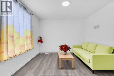 A living room with a green couch, a wooden table with a vase of red flowers, and a window with a yellow and pink curtain.
