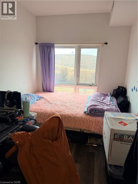 A bedroom with a bed, a window with a purple curtain, and a white fridge.