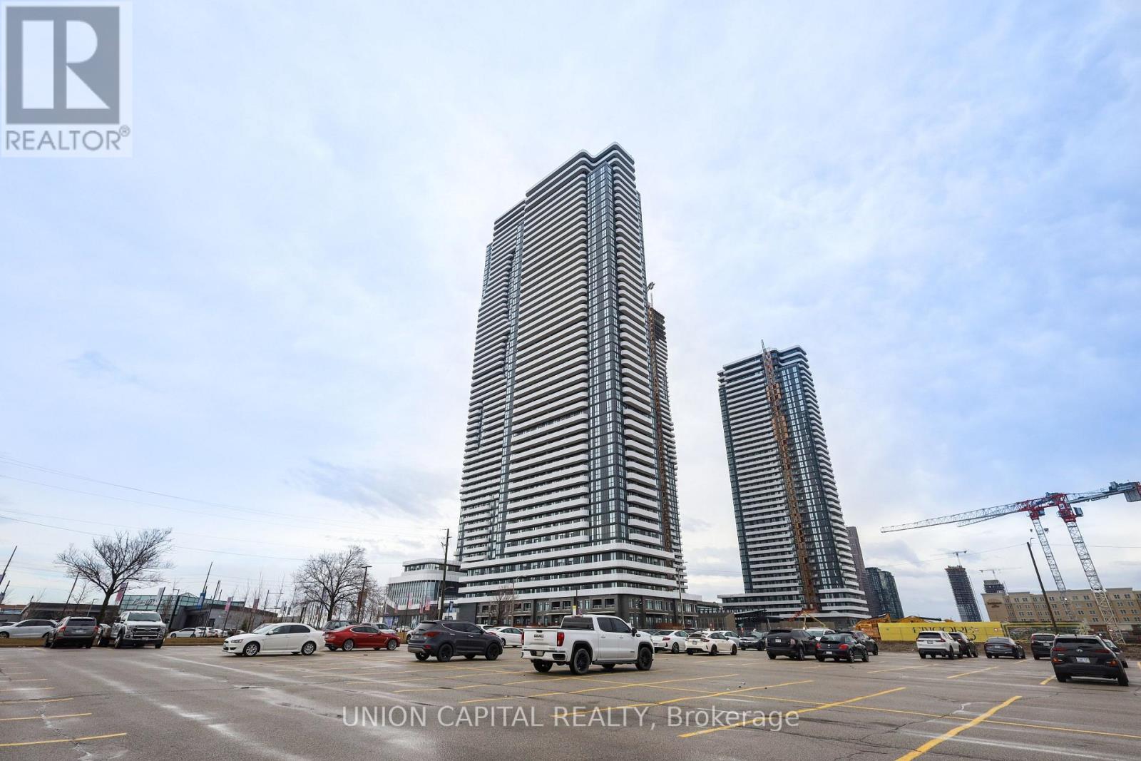 A parking lot with cars and two tall buildings in the background.