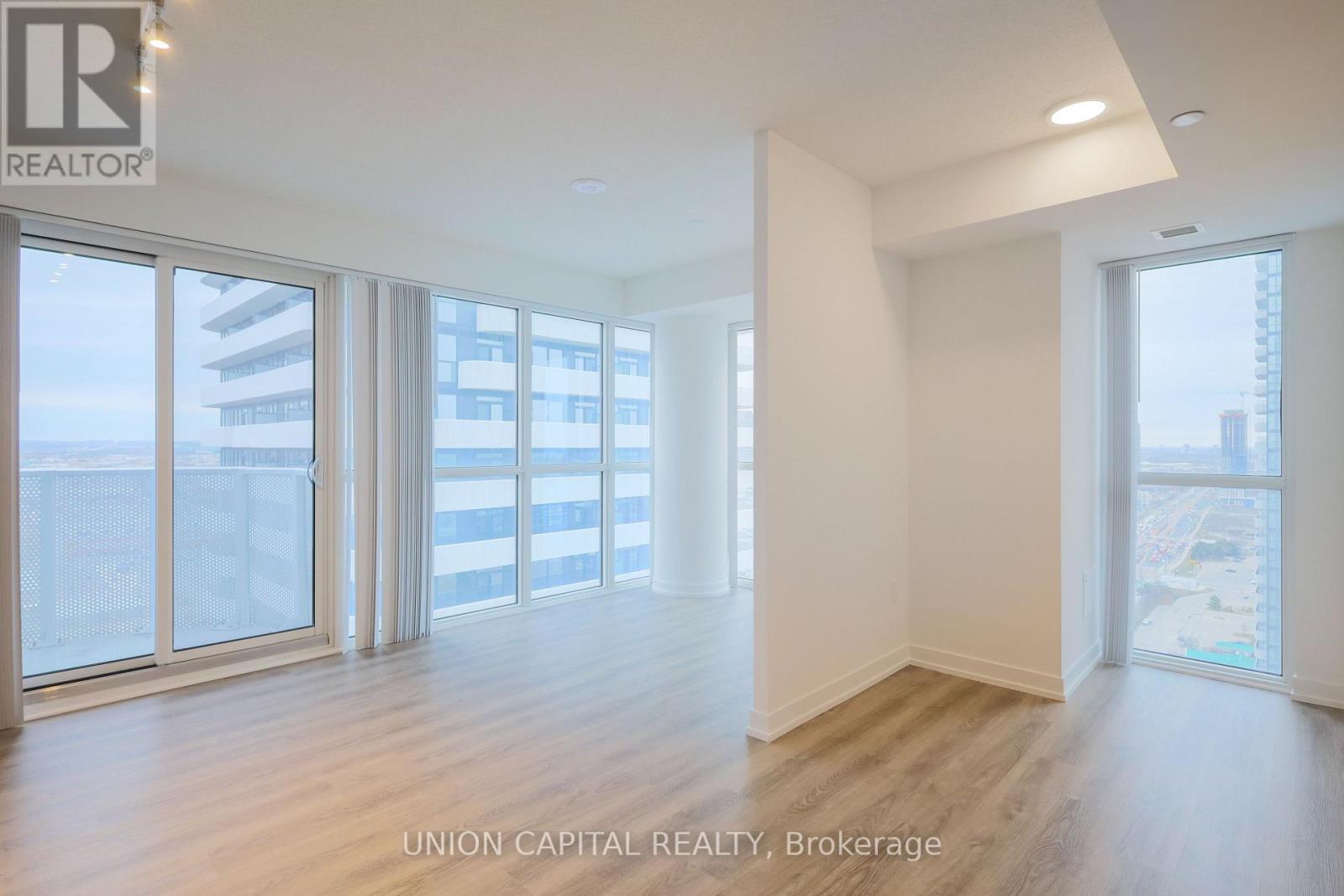 A spacious room with wooden floors and large windows overlooking a cityscape.