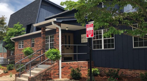 A red and white sign is on a pole in front of a black building.