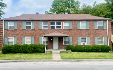 A red brick house with green shutters and a grey door.