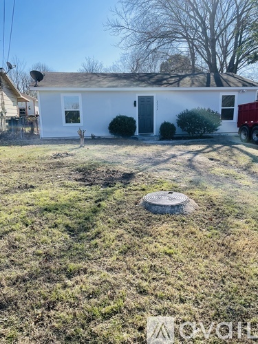 A white house with a black door and a small yard with a manhole cover in the center.