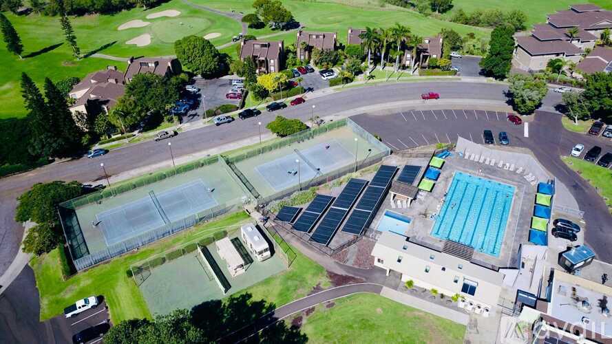 A large swimming pool is surrounded by a grassy area and a parking lot.