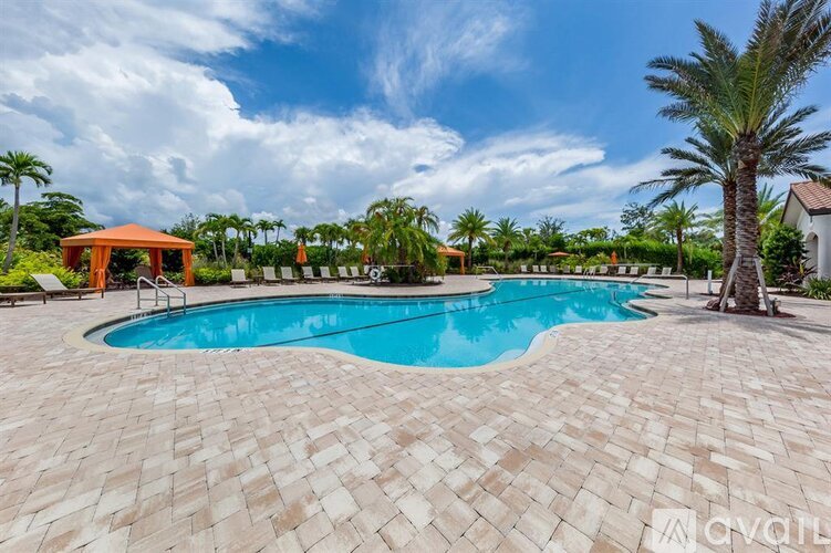 A large outdoor swimming pool surrounded by a brick patio and palm trees.