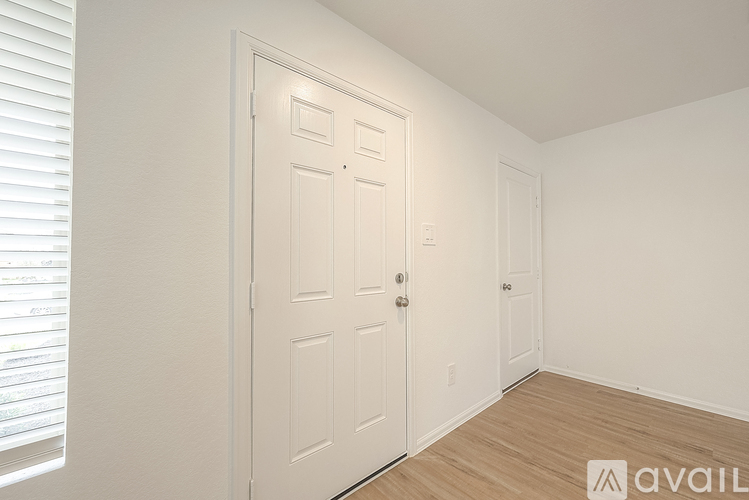 A white door in a room with wooden flooring and a window with blinds.