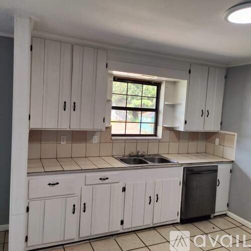 A kitchen with white cabinets and a window.