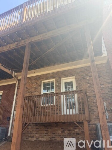 A wooden balcony with a metal railing is attached to a brick building.