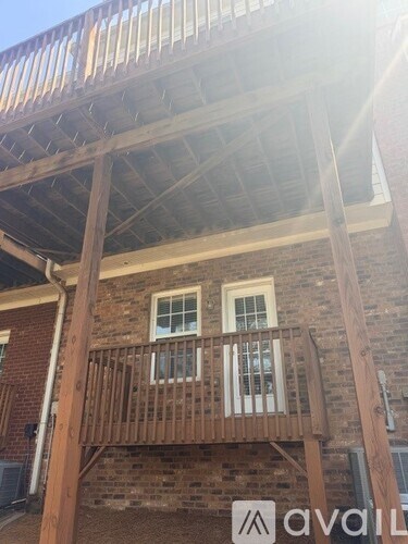 A wooden balcony with a metal railing is attached to a brick building.