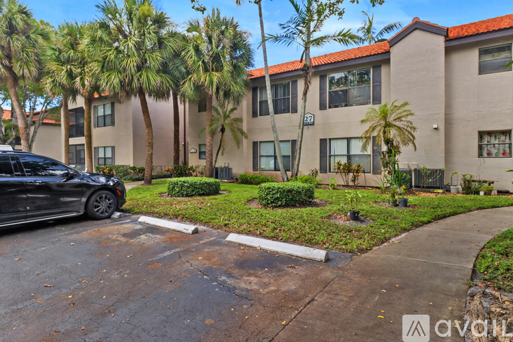 A black car is parked on a street in front of a building with palm trees.