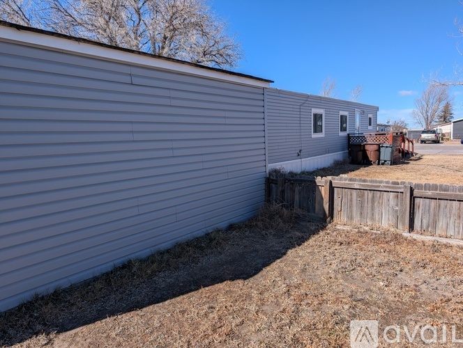 A grey house with a fence and a trash can in front.