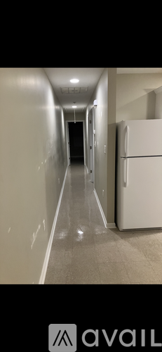 A long hallway with a white refrigerator on the right side.