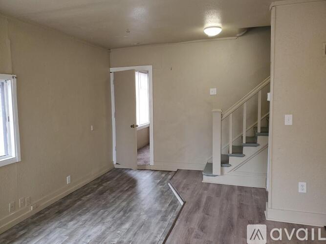 A spacious room with wooden flooring and a staircase leading to another room.