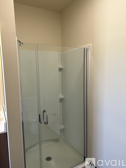 A glass shower stall with a door and a drain.