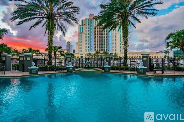 A pool surrounded by palm trees and a large building in the background.