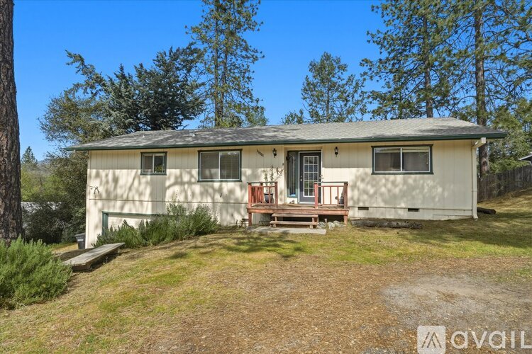 A house with a porch and a red chair is surrounded by trees.
