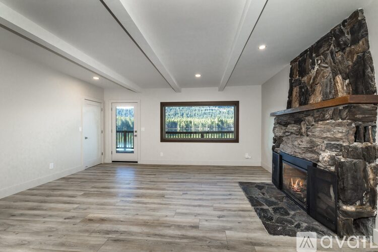 A spacious room with a stone fireplace and a large window showing a view of trees.