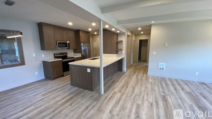 A kitchen with wooden floors and a countertop with a refrigerator, microwave, and oven.