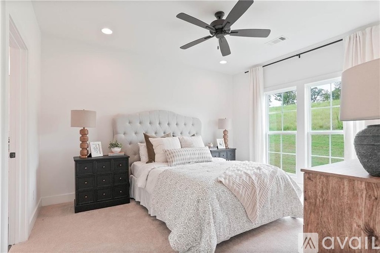 A bedroom with a large bed, a ceiling fan, and a dresser with a lamp on top.