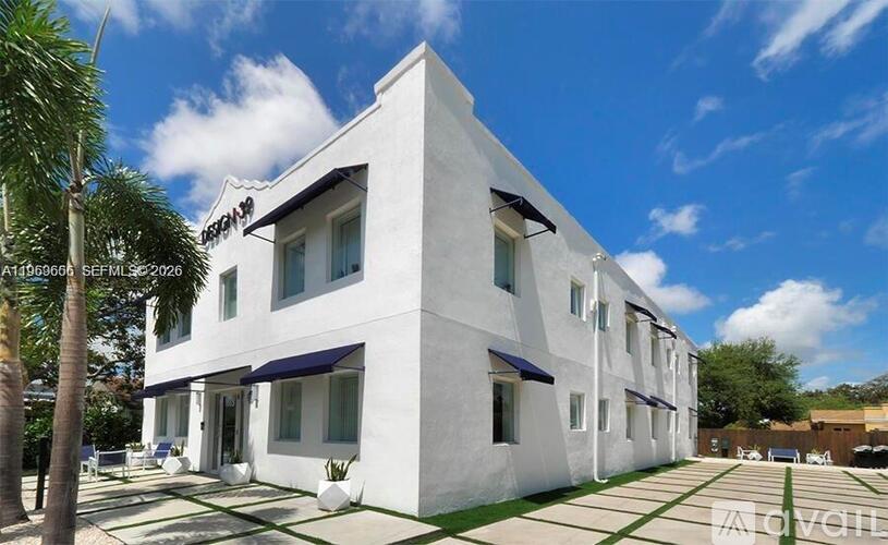 A white building with a blue awning and a palm tree in front.