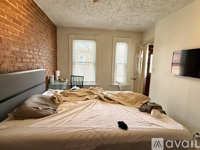 A bedroom with a bed in the center and a brick wall on the left side.