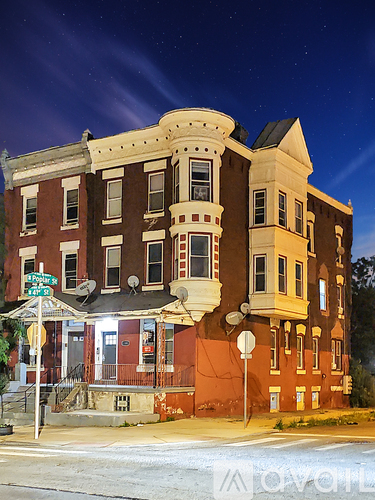 A large, two-story building with a red and brown facade stands on a street corner at night.