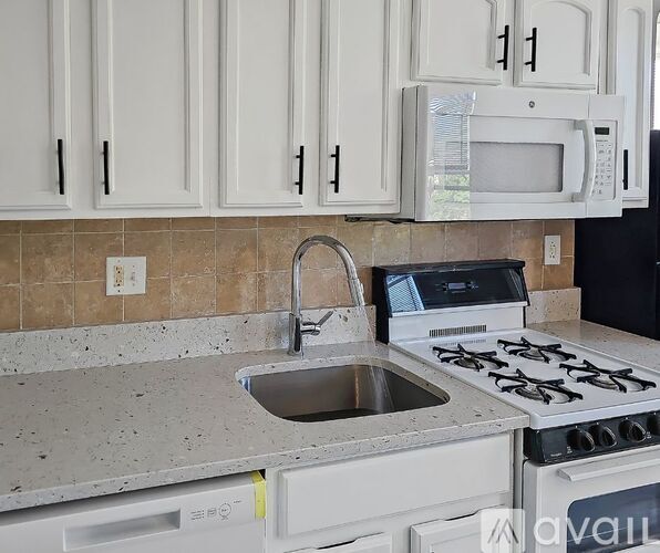 A kitchen with a white stove, sink, and cabinets.
