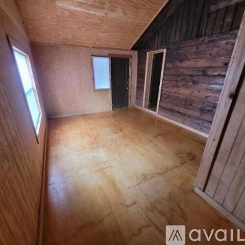 A room with wooden walls and floors, a door, and a window.