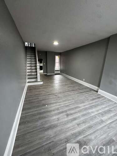 A spacious room with wooden flooring and a staircase on the left side.