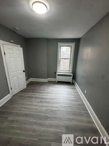A room with a white door and a window with a radiator beneath it.