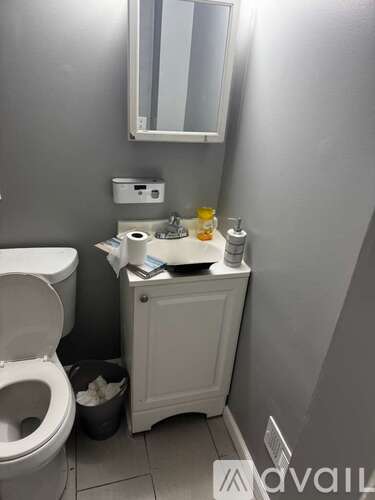 A bathroom with a toilet, a cabinet with a mirror above it, and a trash can.