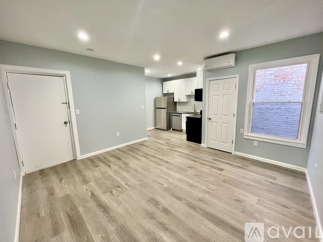 A room with light grey walls and a wooden floor with a white door and a window.