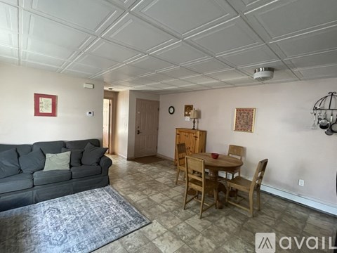 A living room with a grey couch, wooden chairs, and a rug.