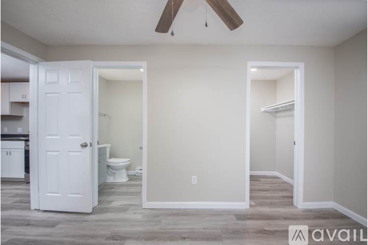 A room with a white door and a toilet in the background.