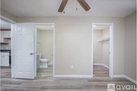 A room with a white door and a toilet in the background.