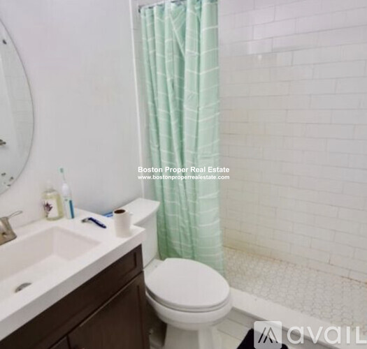A white toilet in a bathroom with a green shower curtain.