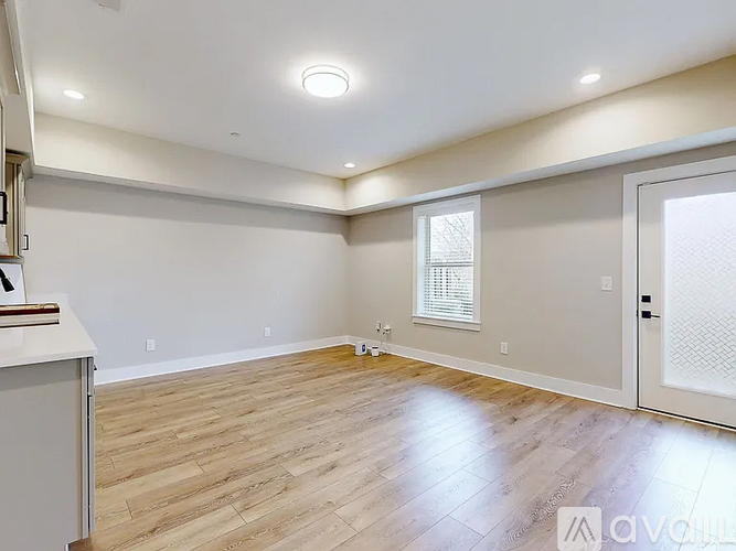 A spacious room with wooden flooring and a window with blinds.