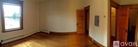 A room with wooden floors and white walls, with a window on the left side.