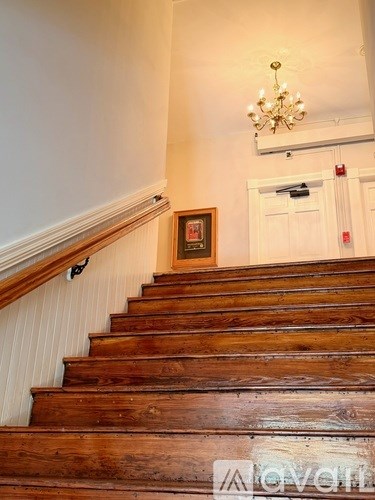 A wooden staircase with a chandelier and a framed picture on the wall.