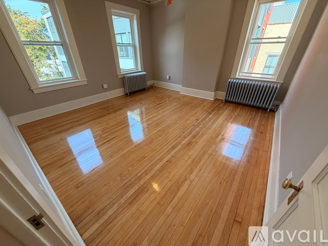 A room with wooden flooring and two windows.