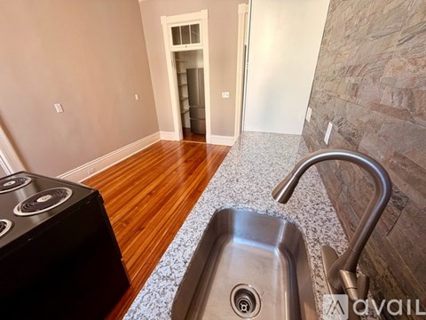 A kitchen with a stove, sink and a stone wall.