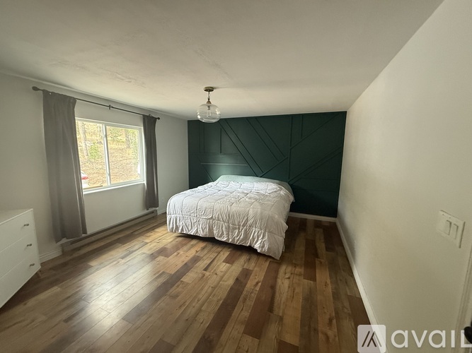 A bedroom with a bed, wooden floors, and a window with curtains.